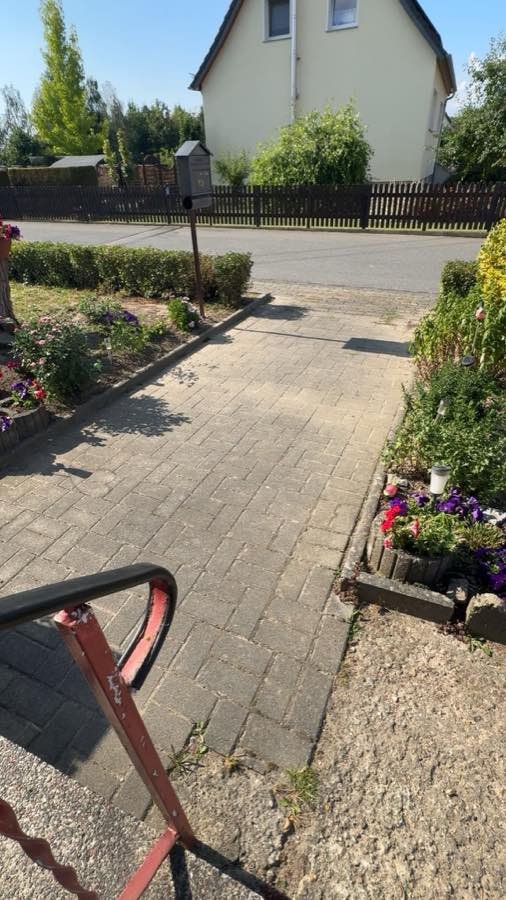 Hofeinfahrt zur Straße vor der Reinigung, das Pflaster ist grau verblasst und an den Rändern bewachsen.
